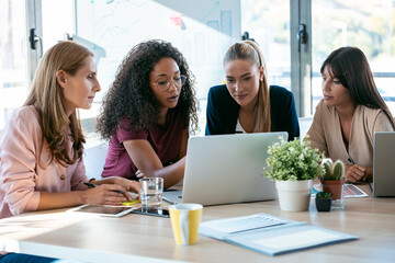 Four beautiful smart business women work with laptops on the desk in the coworking space in the...