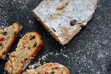 Traditional homemade German Weihnachtsstollen (Christmas stollen or cake) on a slate plate, powdered sugar on top, sliced, filled with candied fruits, raisins, ground almonds and hazelnuts