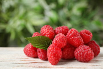 Delicious fresh ripe raspberries with green leaf on white wooden table