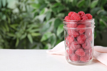 Delicious fresh ripe raspberries in glass jar on white wooden table. Space for text
