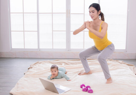 Asian Mother Workout After Delivery Newborn Baby, Young Mom Watching Videos Training Lose Weight Yoga Sport By Computer Laptop,  Beautiful Women And Toddler Infant Play Together With Love And Caring