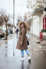 Naklejka premium Portrait of a curly-haired young woman who walks the streets of the city. The girl turns around and smiles