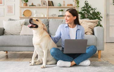 Lady sitting at home with laptop and happy dog