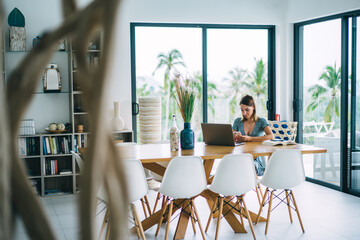 Serious caucasian female student concentrated on learning online using gadgets for online educational course at home, pensive woman freelancer checking remote job project sitting at apartment interior