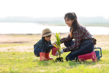 Naklejka na ściany i meble Asian family mom and kid daughter plant sapling tree outdoors in nature spring for reduce global warming growth feature and take care nature earth. 