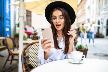 Portrait of young businesswoman drinking coffee and using mobile phone while sitting at the...