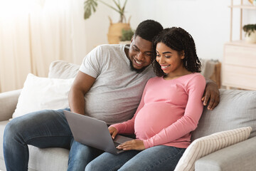 Obraz premium Happy black expecting family using laptop at living room