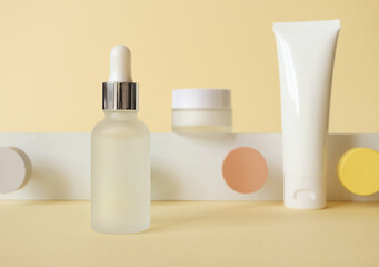 Facial skincare beauty cosmetic products on pastel yellow background and geometrical decor, front view. Serum in glass bottle, moisturizer cream and facial cleanser in plastic tube