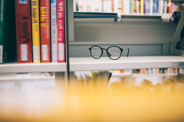 Selective focus on trendy optical spectacles for provide eyes protection staying on shelf bookcase in university library, stylish classic eyewear for vision correction near literature best sellers