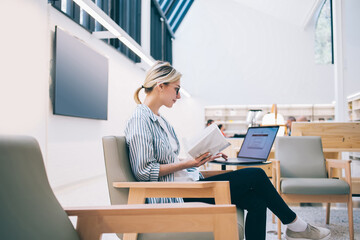 Skilled female freelancer installing app for doing distance job holding literature book for reading...