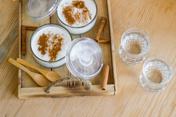 Fototapeta na wymiar Traditional Turkish Rice Pudding in stylish glass bowls on wooden tray with cinnamon sticks and wooden spoons