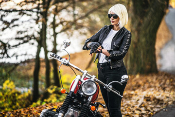 Naklejka na ściany i meble Pretty blonde biker girl in sunglasses with red motorcycle on the road in the forest