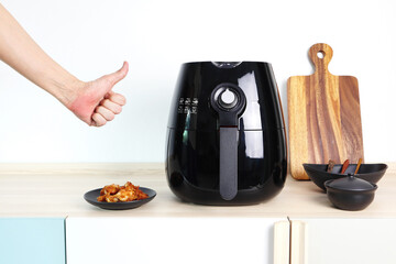 a black deep fryer or oil free fryer appliance, mug, dish and wooden tray are on the wooden table...