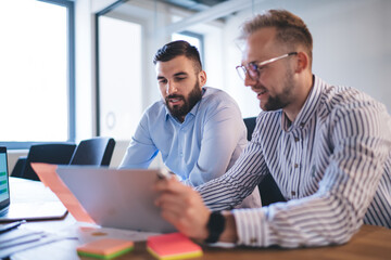Serious professional male entrepreneur discussing finance report with clever manager on meeting, businessmen reading information about project communicating and share opinions