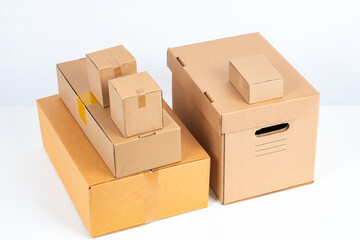 Cardboard boxes of different types stand on top of each other. Cardboard boxes for storage and transportation. Unlabeled boxes on a white background. Production and sale of packaging materials.