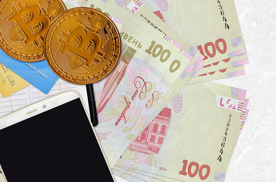100 Ukrainian hryvnias bills and golden bitcoins with smartphone and credit cards. Cryptocurrency investment concept. Crypto mining or trading