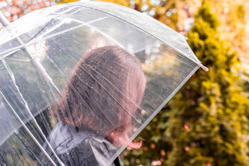 Autumn. Lonely sad redhead woman walking in a park, garden. View through wet  transparent umbrella with rain drops. Rainy day landscape. Vintage Toned
