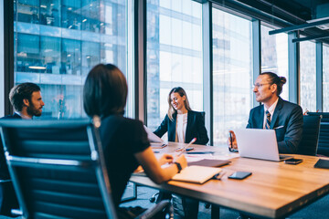 Prosperous team of financial experts in elegant formal wear discussing business planning during...