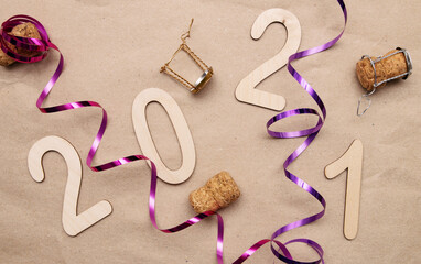 Light wooden 2021 numbers lie randomly on craft paper with champagne corks, packing tape and muzlet
