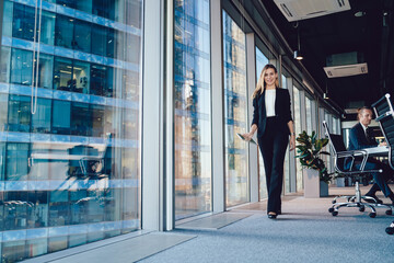 Cheerful elegant businesswoman walking with tablet in boardroom