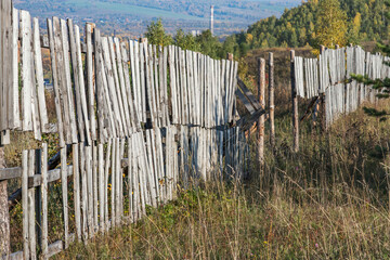 An old wooden fence to protect against snow drifts on a mountain near the city. Travel to Siberia in Russia in autumn.
