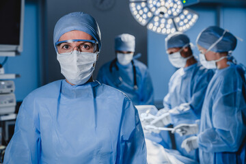 Portrait of female surgeon wearing scrubs and protective glasses in hospital operating theater.