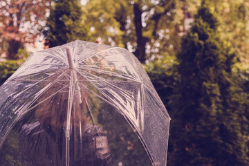 Autumn. Lonely redhead girl under a transparent umbrella with rain drops walking in a park, garden. Rainy day landscape