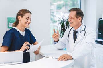 Senior doctor talking with nurse receptionist at hospital reception