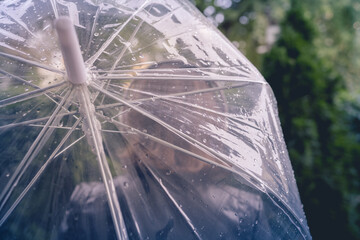 Autumn. Lonely sad woman in a headphones walking in a park, garden. View through wet  transparent umbrella with rain drops. Rainy day landscape. Vintage Toned