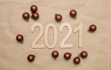 Light wooden numbers 2021 lie in the center on craft paper with new year round brown balls