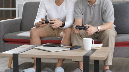 Fototapeta premium Asian two age generations men family old father embracing young adult son having fun enjoying play video game funny video using at home sit on sofa. Happiness Asian family concepts.