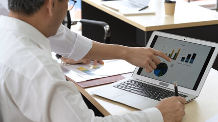 Close up of two asian young businessmen using laptop at working together. Creative business people in modern office. Two men discussing marketing plan. Laptop and paperwork on the table.