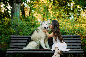 Young dwarf woman sits on bench next to Malamute dog and hugs it.