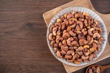 Cashew nuts with peel in a plate on wooden tray and table background, healthy raw food plate.