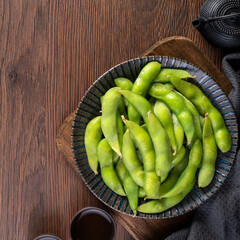 Fresh cooked boiled edamame in a plate on wooden tray and table background, healthy protein food concept.