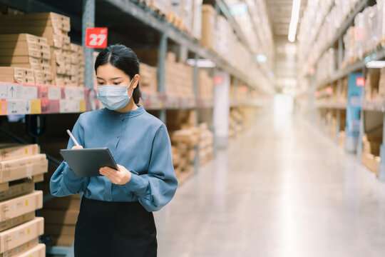 Young smart Asian business working woman wear surgical mask  using digital tablet to check goods on shelves for inventory management  in warehouse, Logistics business planning concept with copy space