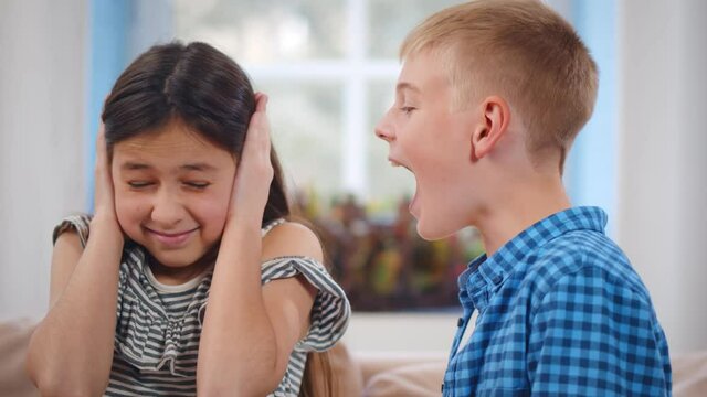Irritated girl closing ears with hands while brother yelling at her