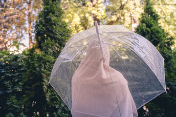 Autumn. Lonely muslim woman in a headscarf under a transparent umbrella with rain drops walking in a park, garden. Rainy day landscape. Vintage Toned