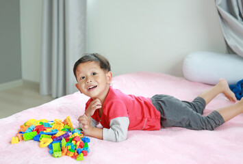 Adorable asian little baby boy playing colorful plastic blocks and lying on bed.