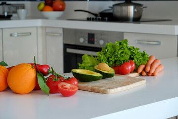 Bunch of veggies and greens laid on white countertop. Avocado, lettuce salad leaves, tomatoes and other vegetables on kitchen table. Vegan diet concept. Close up, copy space, background, top view.