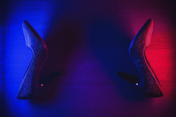Black high heels shoes in the neon lights on black background.
