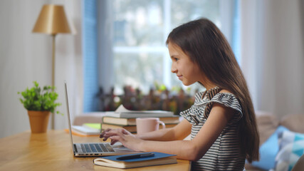 Pretty concentrated schoolgirl studying at home using laptop.