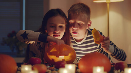 Kids carving pumpkin on Halloween at home sitting at table in living room