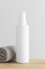 Obraz na płótnie Canvas White cosmetic lotion bottle mockup with a towel on a wooden table.