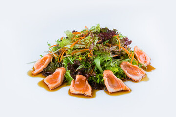 Pan Asian salad with salmon Tataki fillet, herb salad mix isolated on white background. Side view of fresh fish salad with carrot slices and soy sauce. Restaurant menu dish isolation