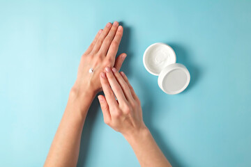 Revitalizing hand cream for healing and recovery after excessive use of soap and disinfectants. Young woman applying moisturizing lotion. Copy space, close up, pink background, flat lay, top view.