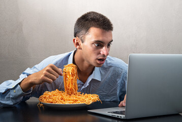 man eating spaghetti with tomato sauce and watching the computer