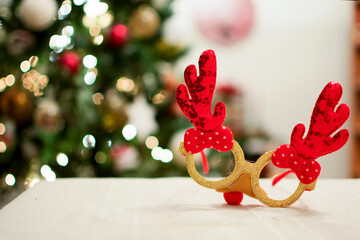 Some funny glasses with red Christmas reindeer antlers, in the background the lights of the Christmas tree.