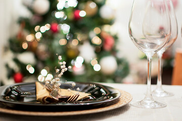 Wine glasses, plate and cutlery prepared on the Christmas table, with the Christmas tree in the background.
