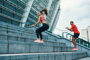 Fototapeta na wymiar Beautiful young couple in sports clothing jumping on stairs outdoors